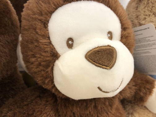 A close-up of a plush toy with soft, brown fur and a white face. It has embroidered eyes and nose, and a gentle, smiling expression. The texture appears fluffy and inviting.
