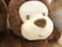 A close-up of a plush toy with soft, brown fur and a white face. It has embroidered eyes and nose, and a gentle, smiling expression. The texture appears fluffy and inviting.