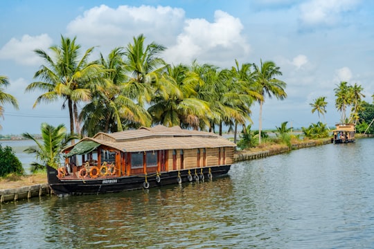 brown wooden boat on body of water near green palm trees during daytime in Alappuzha India