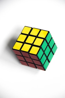 A Rubik's Cube with visible sides showing yellow, green, and red squares on a white background. The cube is rotated, displaying three sides, and appears to be in a solved state.