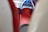 A close-up view of a patterned, red upholstered seat with blue headrest sections, likely on public transport. The background includes parts of a window and other blurred seats.