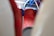 A close-up view of a patterned, red upholstered seat with blue headrest sections, likely on public transport. The background includes parts of a window and other blurred seats.