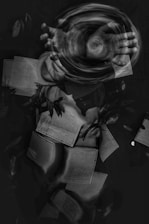 A swirling motion created by a pair of hands in the center gives the impression of manipulating energy or air. Surrounding the hands, multiple pages filled with text float effortlessly in a dark space, intertwining with abstract elements and subtle plant-like textures.