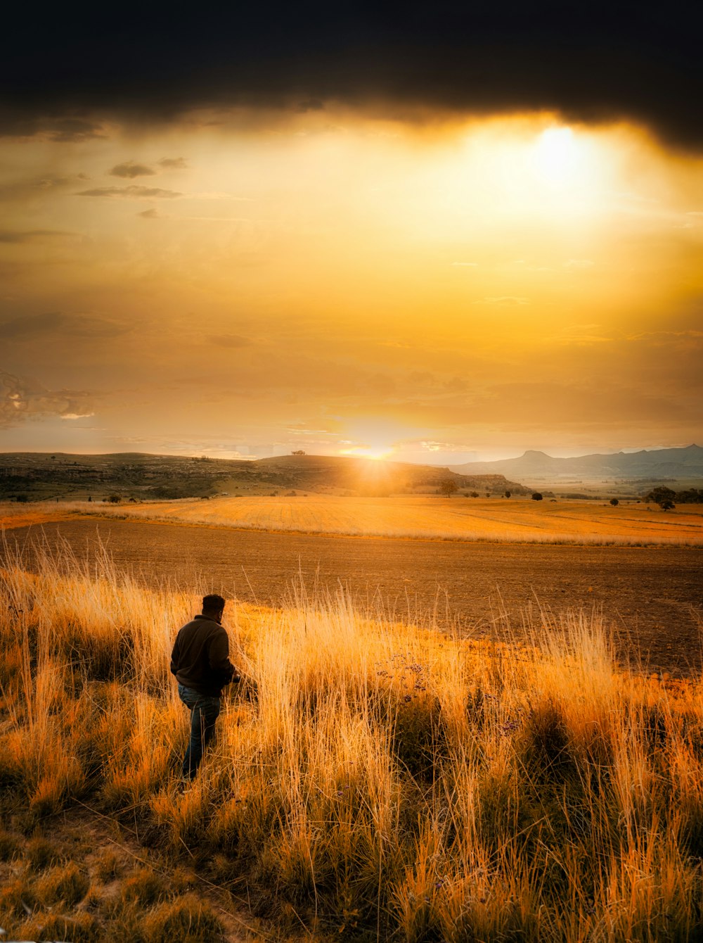 uomo in giacca nera in piedi sul campo di erba marrone durante il tramonto