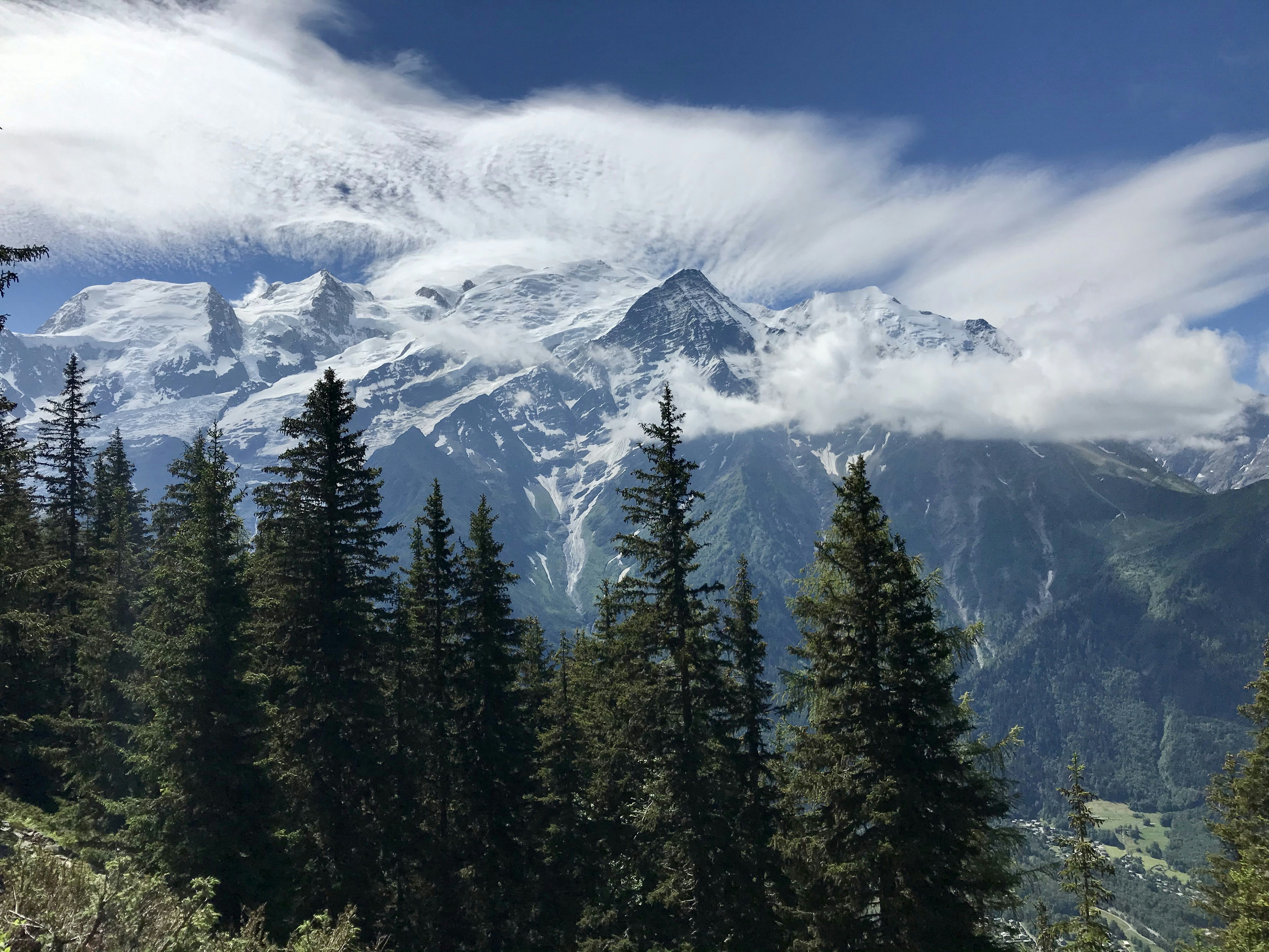 green pine trees near snow covered mountain under white clouds and blue sky during daytime
