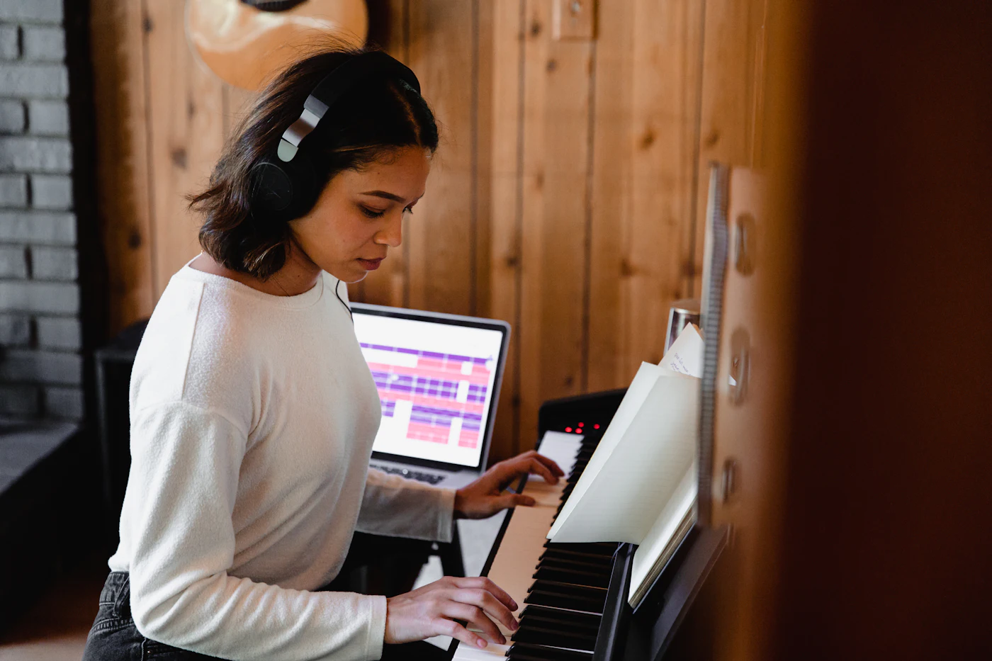 A student playing a digital piano in headphones, with a laptop open beside the keys