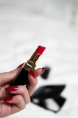A delicate hand adorned with vintage gold rings holding a blush pink lipstick.