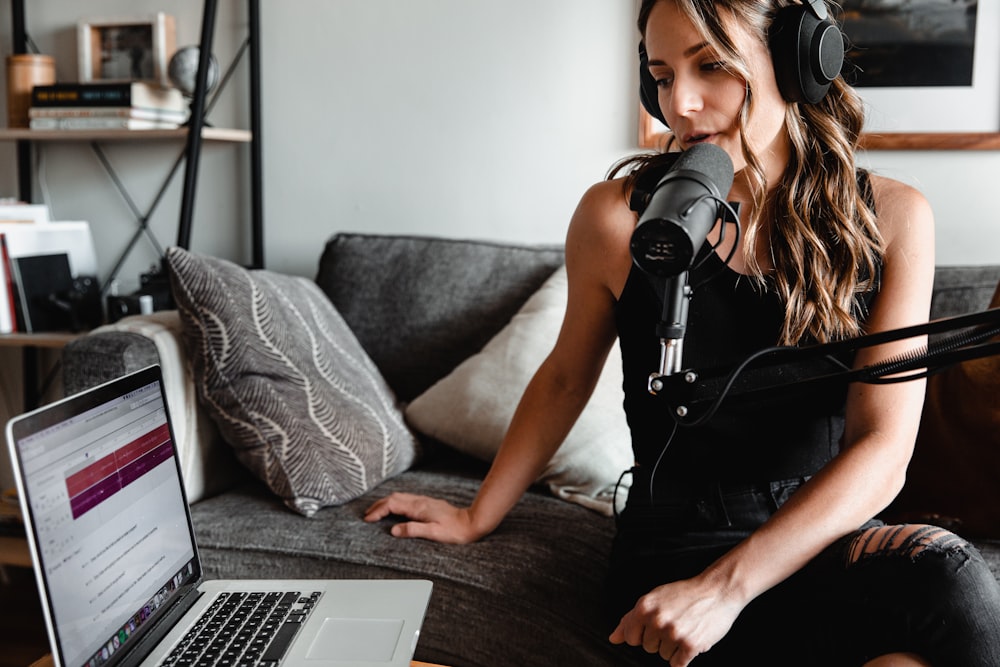 Femme en débardeur noir assise sur un canapé à l’aide d’un MacBook