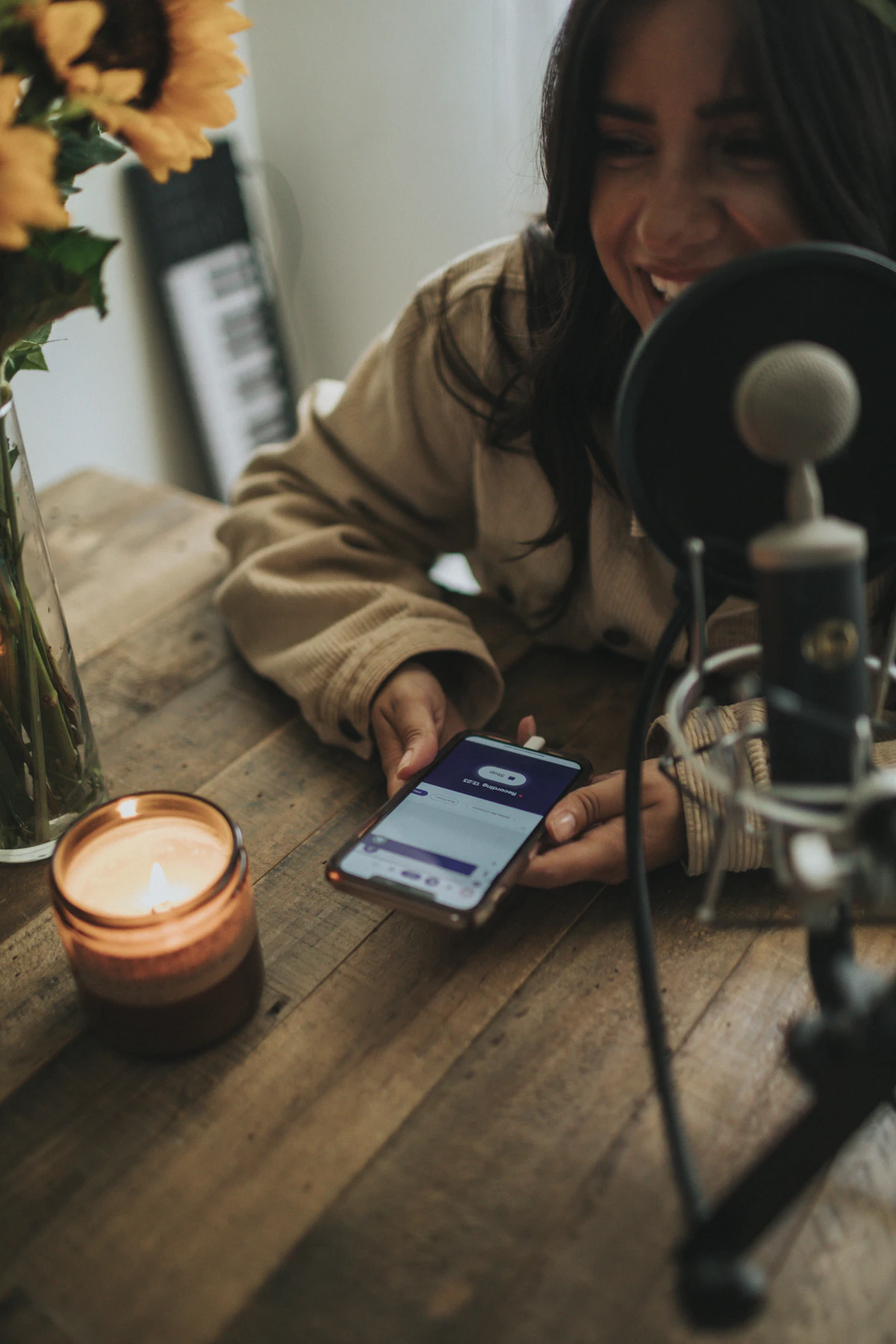 A smiling woman looks at her phone beside a podcast microphone, ready to share her newly published interview