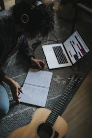 person in black jacket sitting on floor while writing on notebook