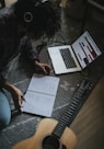 person in black jacket sitting on floor while writing on notebook