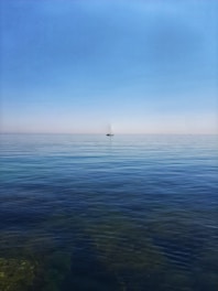 A serene ocean view with a small sailboat gliding under a clear blue sky.