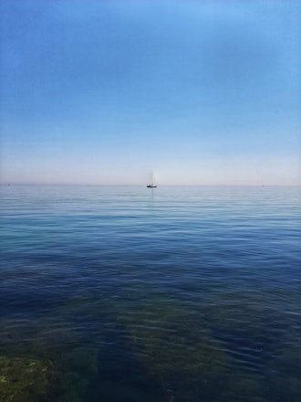 A serene ocean view with a small sailboat gliding under a clear blue sky.