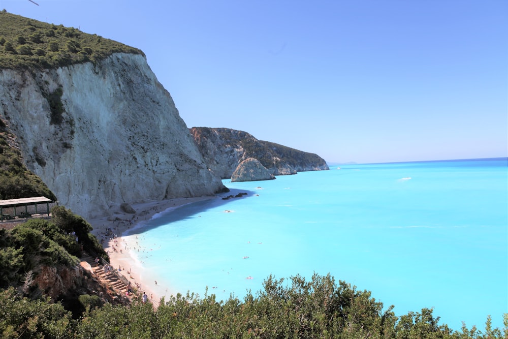 árvores verdes na montanha rochosa marrom ao lado do mar azul sob o céu azul durante o dia