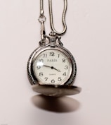An ornate pocket watch with a silver chain is featured. The clock face displays the time and has markings for each hour, with the word 'PARIS' prominently displayed. The cover of the pocket watch is slightly open, revealing the classic watch face.