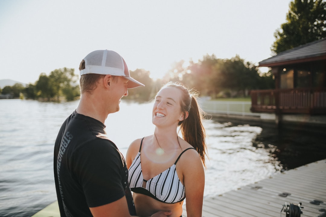 woman in white and black bikini top and white hat standing beside man in black shirt,