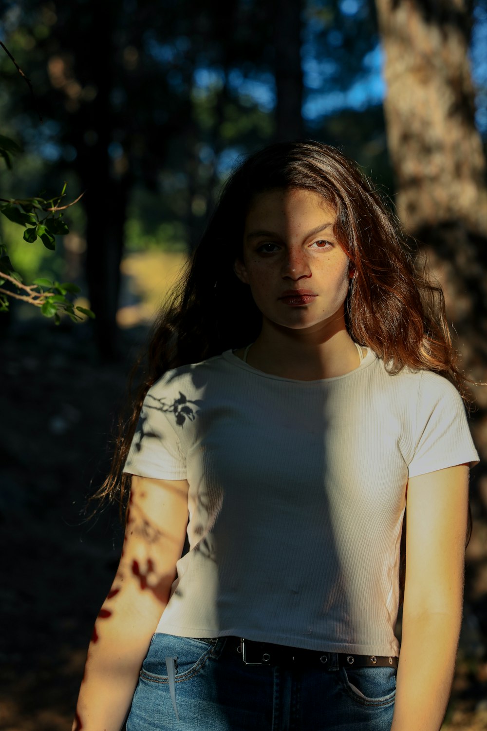 Mujer con camiseta blanca de cuello redondo de pie cerca del árbol durante el día