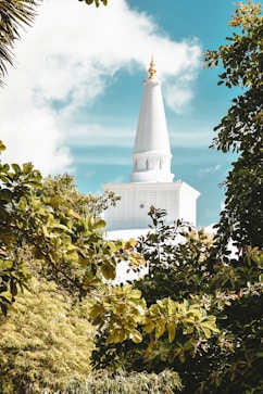 white concrete building near green trees under blue sky and white clouds during daytime