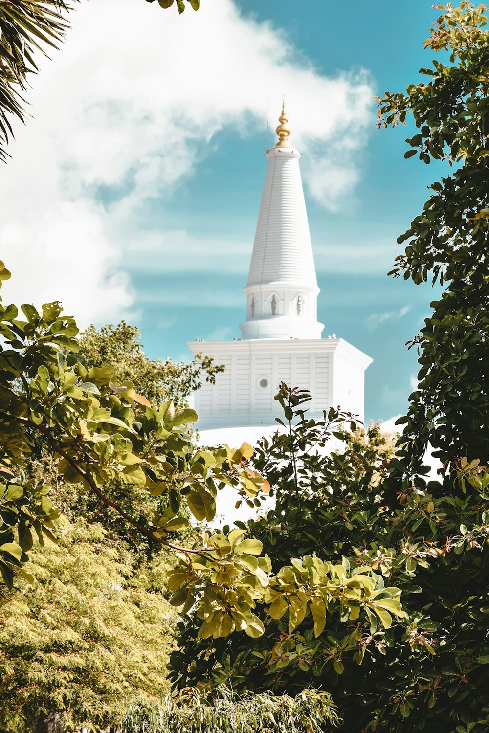 white concrete building near green trees under blue sky and white clouds during daytime