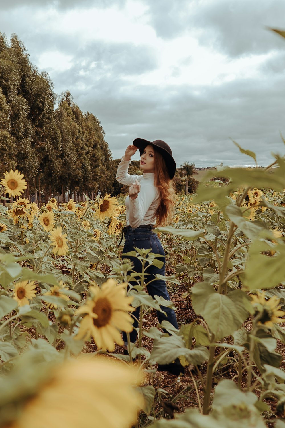 woman in white shirt and blue skirt standing on sunflower field under white clouds and blue