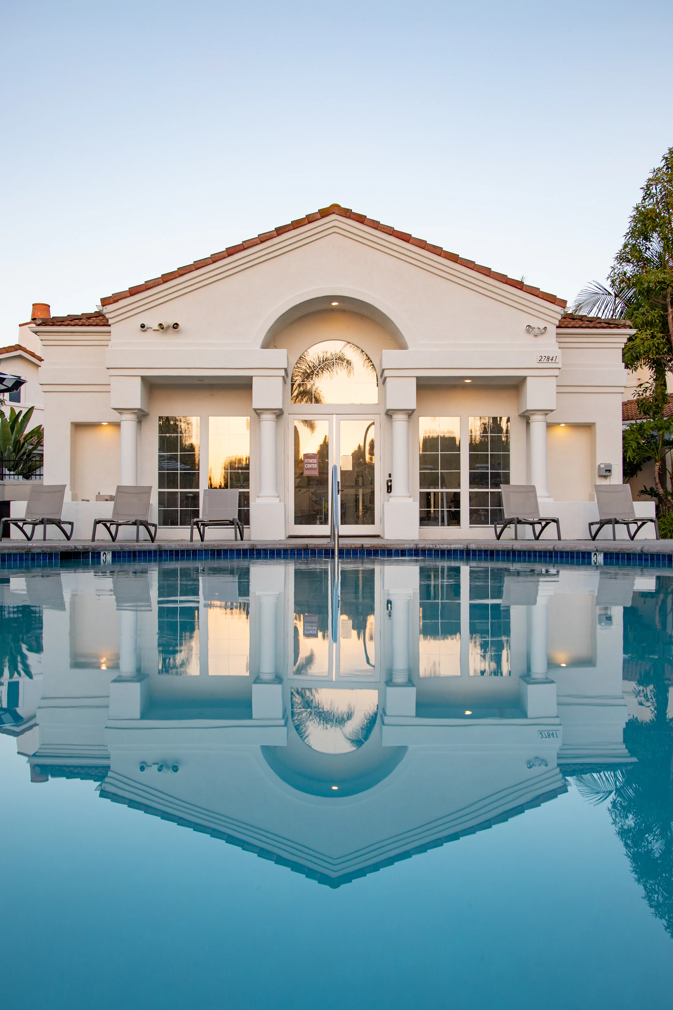 A classical white estate with columns, mirrored in a long still pool