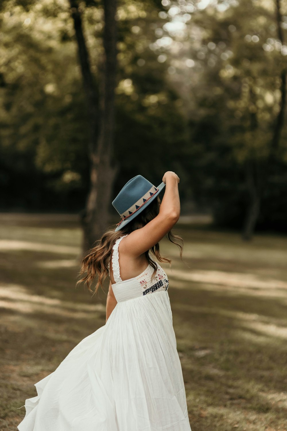 woman in white dress wearing blue fedora hat standing on brown field during daytime