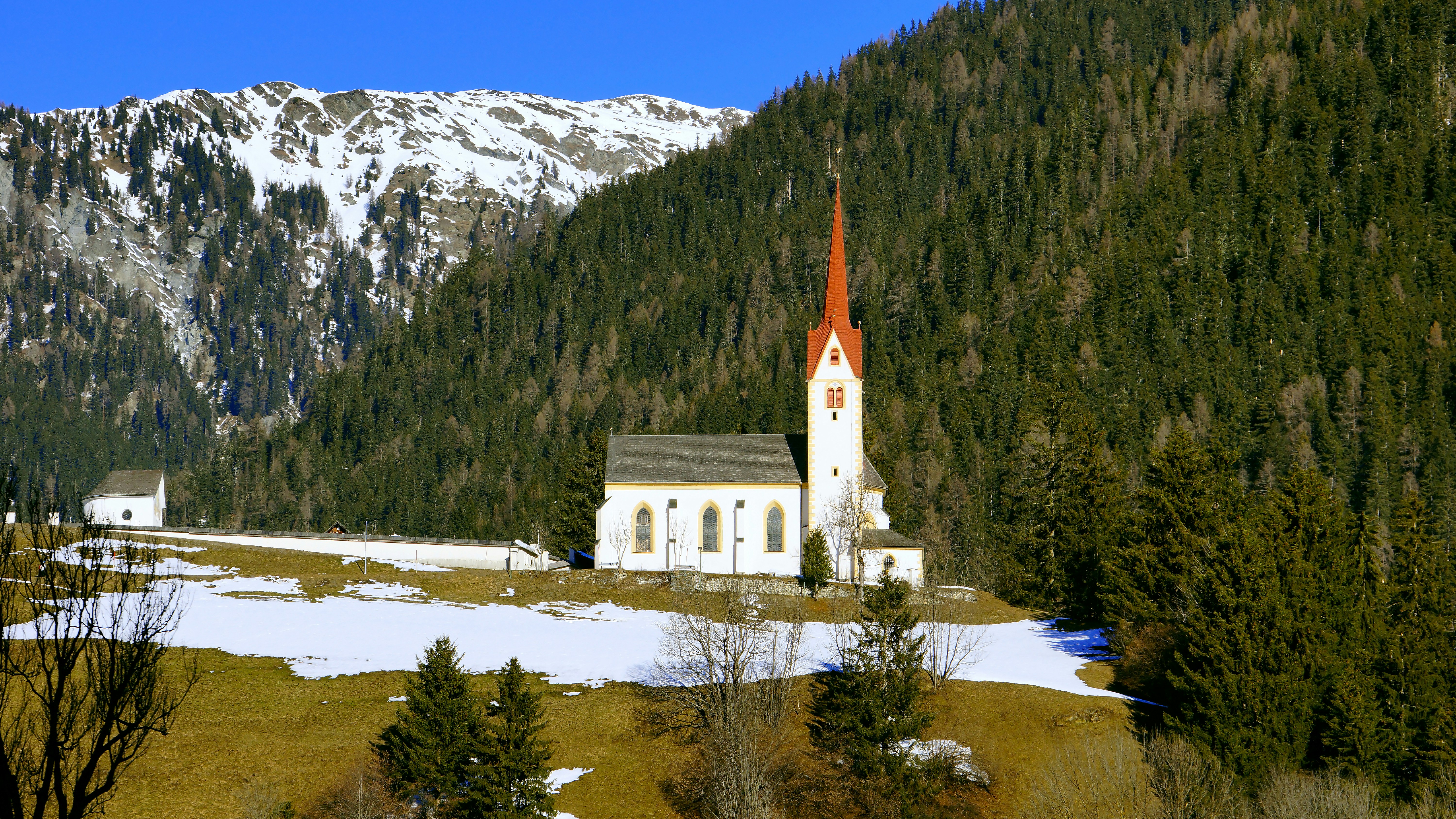 white and brown concrete building near green trees and mountain during daytime