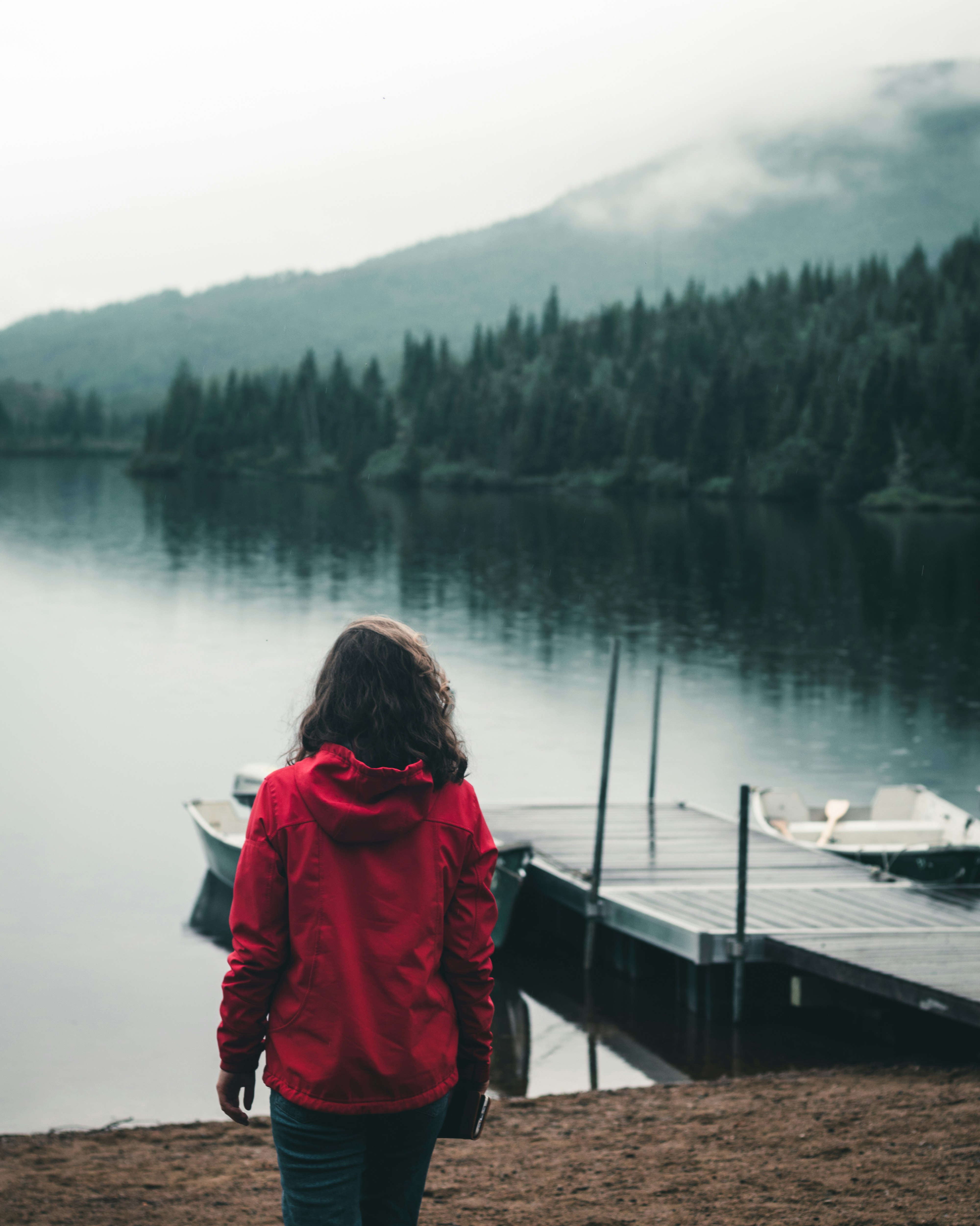 woman in red hoodie standing on dock looking at lake during daytime