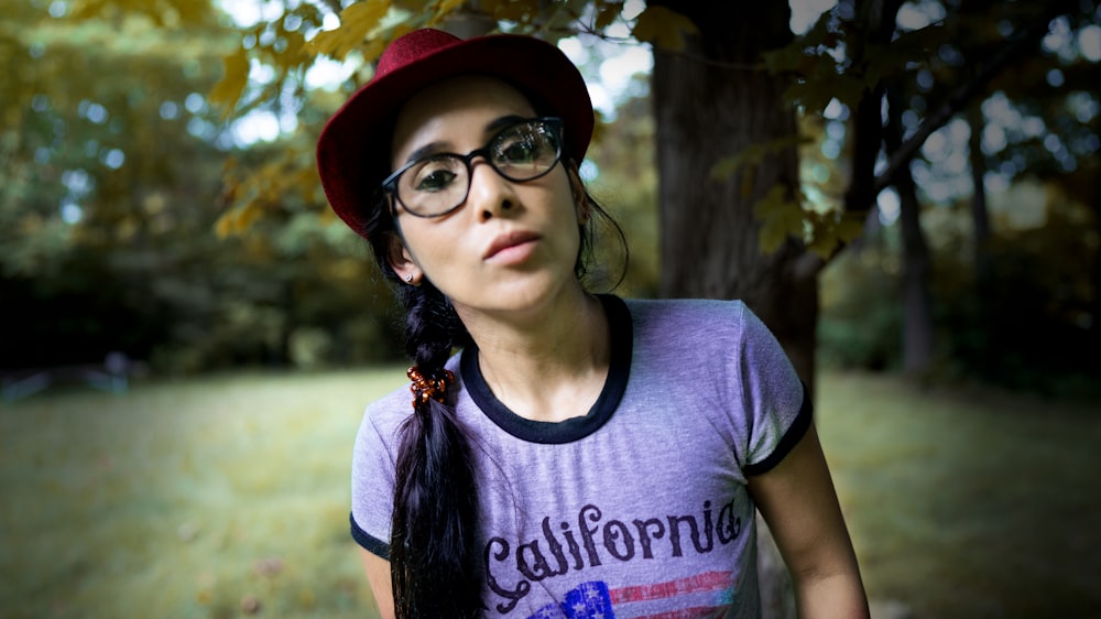 woman in gray crew neck t-shirt wearing black framed eyeglasses and red hat