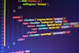 Computer code displayed on a monitor, featuring syntax highlighting. The code appears to be written in JavaScript, with HTML elements indicating a part of a web application. Various tags, class names, and functions are visible, emphasizing a focus on front-end development.