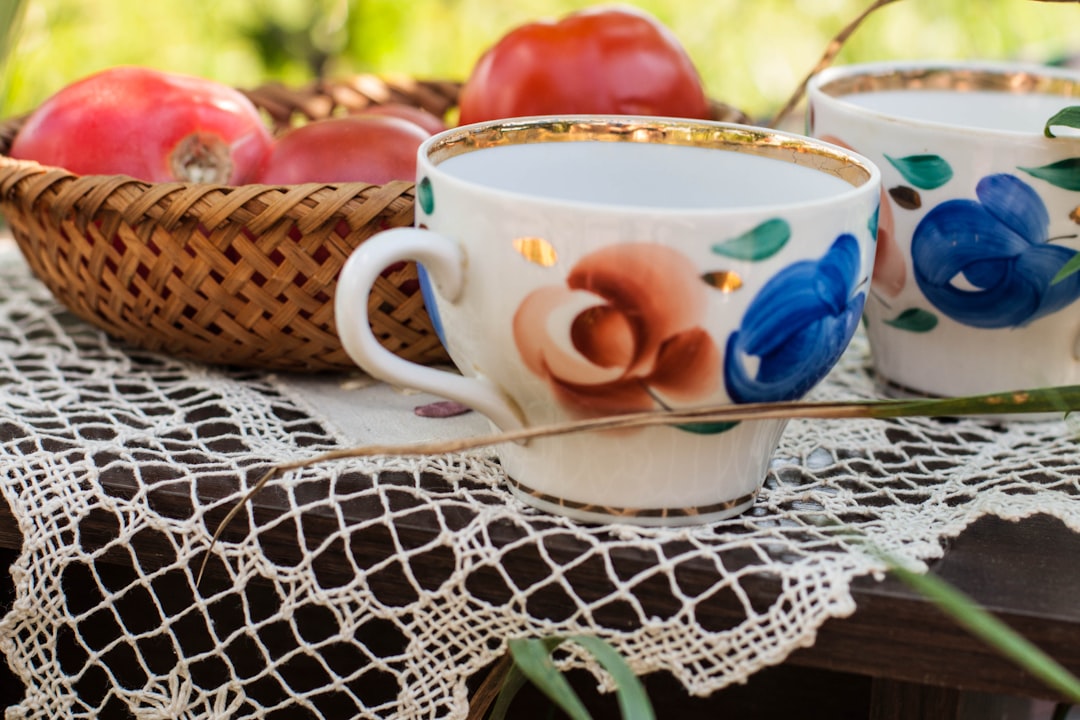 white and pink floral ceramic teacup on white and blue floral table cloth