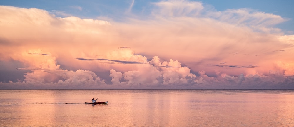 homme chevauchant un bateau sur la mer sous des nuages blancs et un ciel bleu pendant la journée
