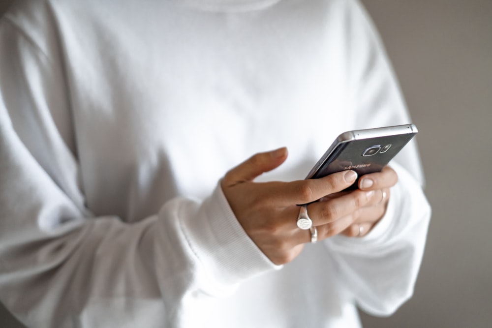 pessoa na camisa branca de manga comprida segurando smartphone preto