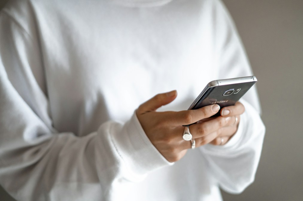 Person in a white shirt holding a smartphone, checking a business messaging app