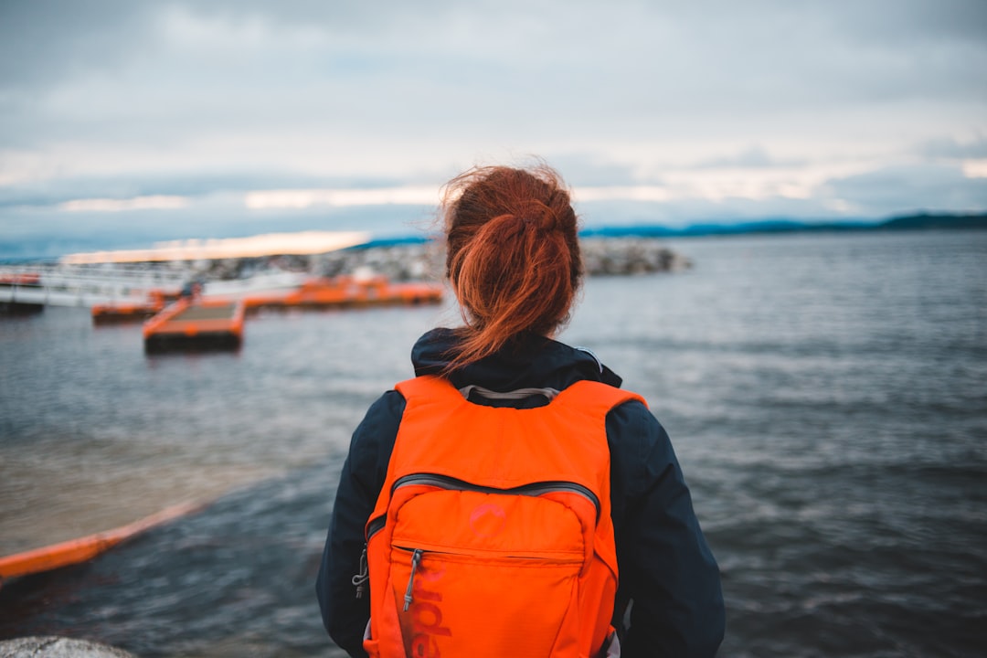 woman in black jacket and orange backpack standing on shore during daytime