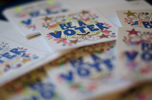 A collection of colorful cards feature the phrase 'Be A Voter' written in bold letters surrounded by decorative stars, swirls, and dots, emphasizing a voting theme.