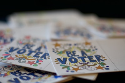 A stack of colorful cards featuring the bold text 'BE A VOTER' surrounded by decorative stars and swirls.