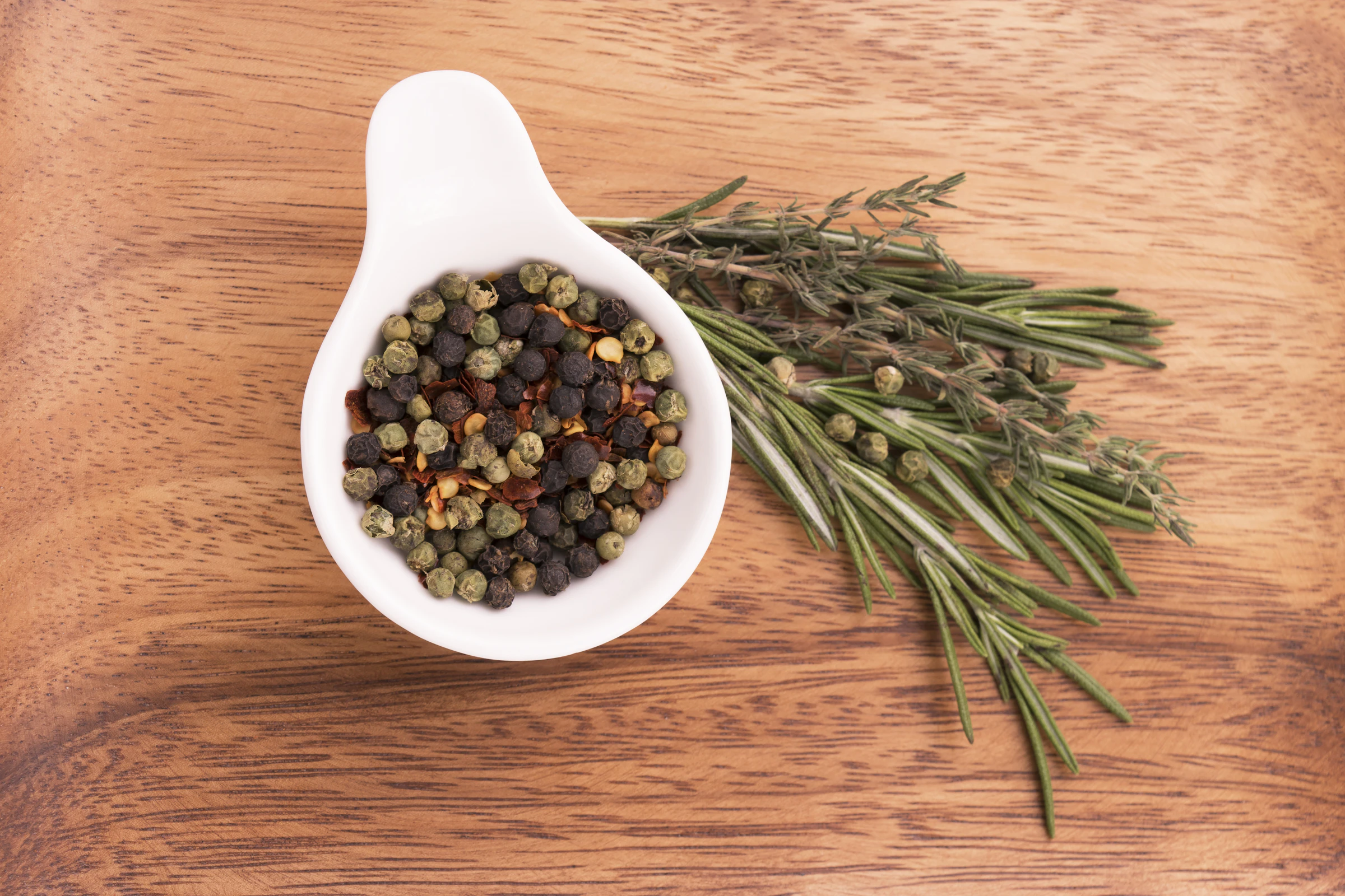 Mixed peppercorns and herbs on a wooden surface