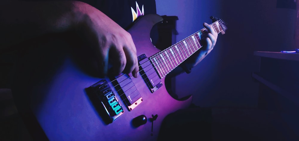 person playing electric guitar with blue background