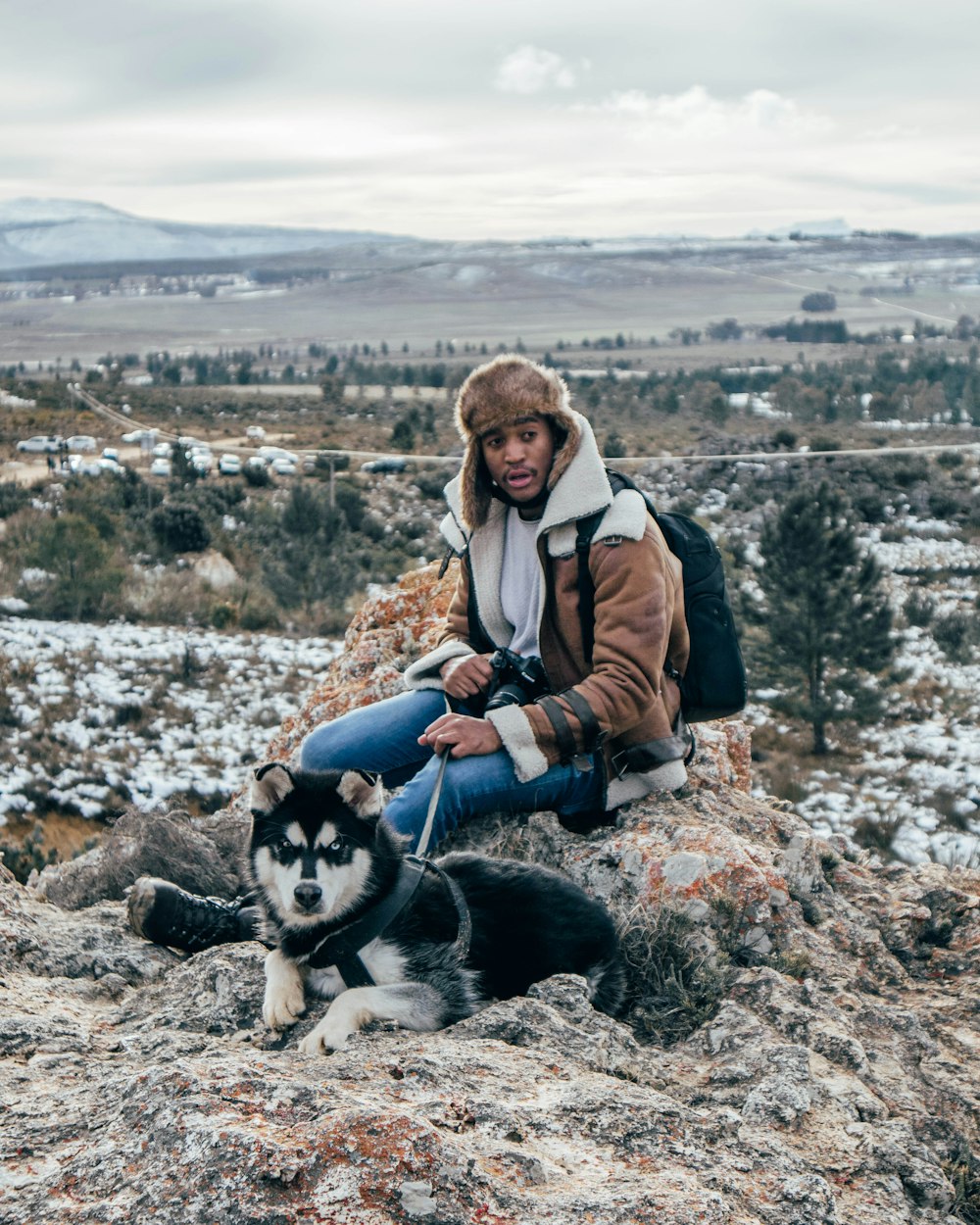 man and woman sitting on rock beside black and white siberian husky during daytime