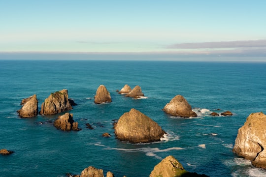 brown rocks on blue sea under blue sky during daytime in Nugget Point New Zealand
