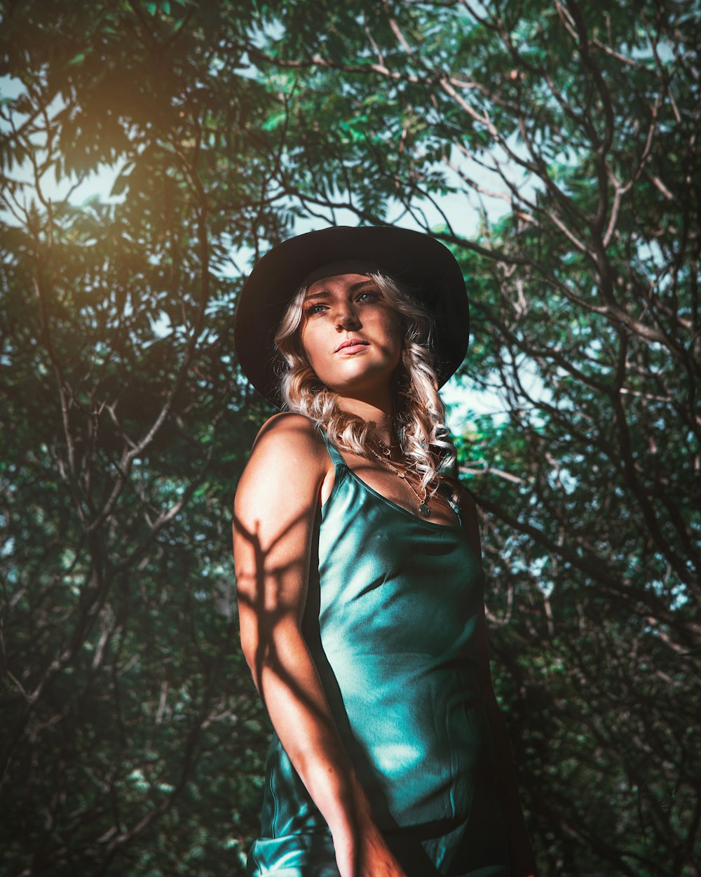 woman in green spaghetti strap dress wearing black hat standing near trees during daytime