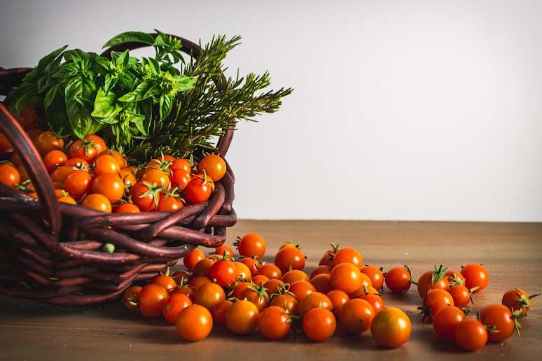 tomatos and green vegetables and herbs on brown woven basket