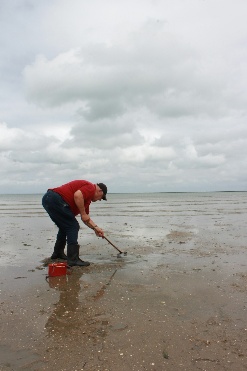 man in blue t-shirt and blue denim jeans holding red and black shovel on beach