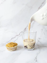 Creamy oat milk pouring into a glass beside fresh eggs and chili peppers