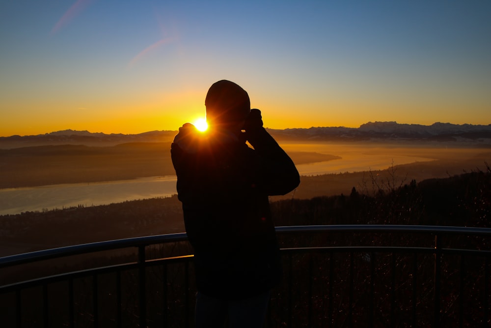 silhouette of man standing near fence during sunset