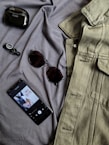 black iphone 4 beside brown framed sunglasses and gray denim button up shirt