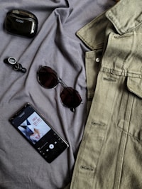 black iphone 4 beside brown framed sunglasses and gray denim button up shirt