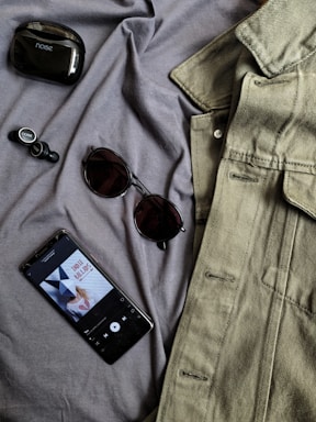 black iphone 4 beside brown framed sunglasses and gray denim button up shirt