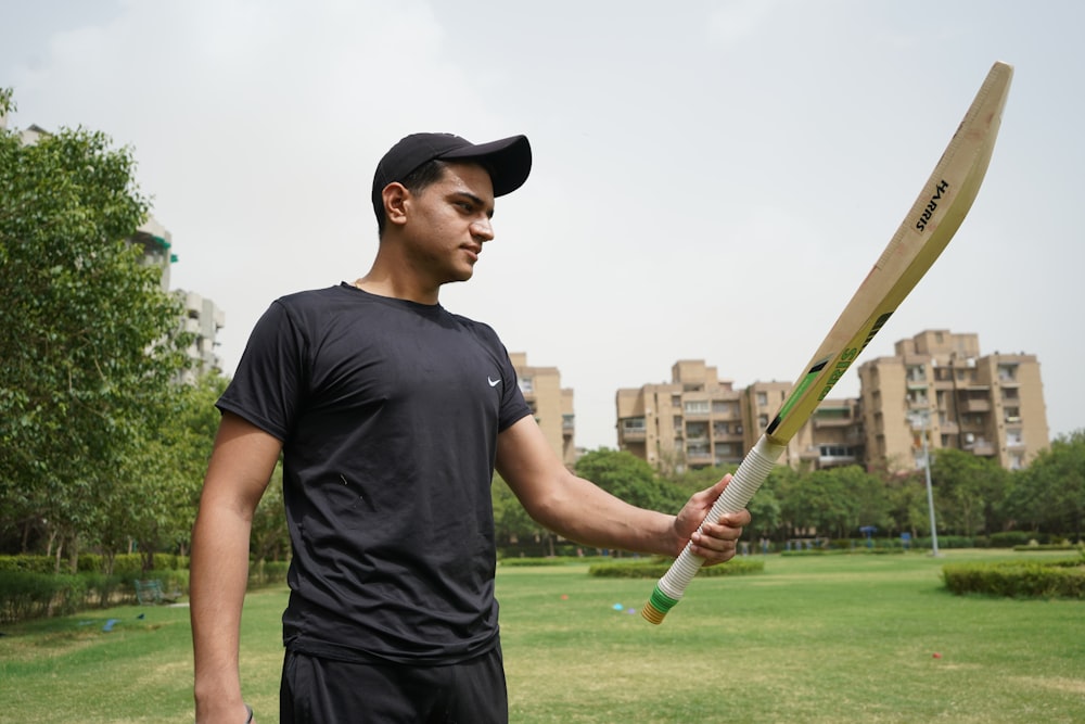 man in black crew neck t-shirt and black cap holding baseball bat